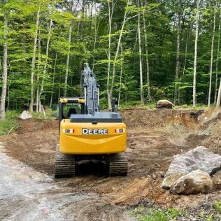 A yellow deere excavator is driving down a dirt road in the woods.