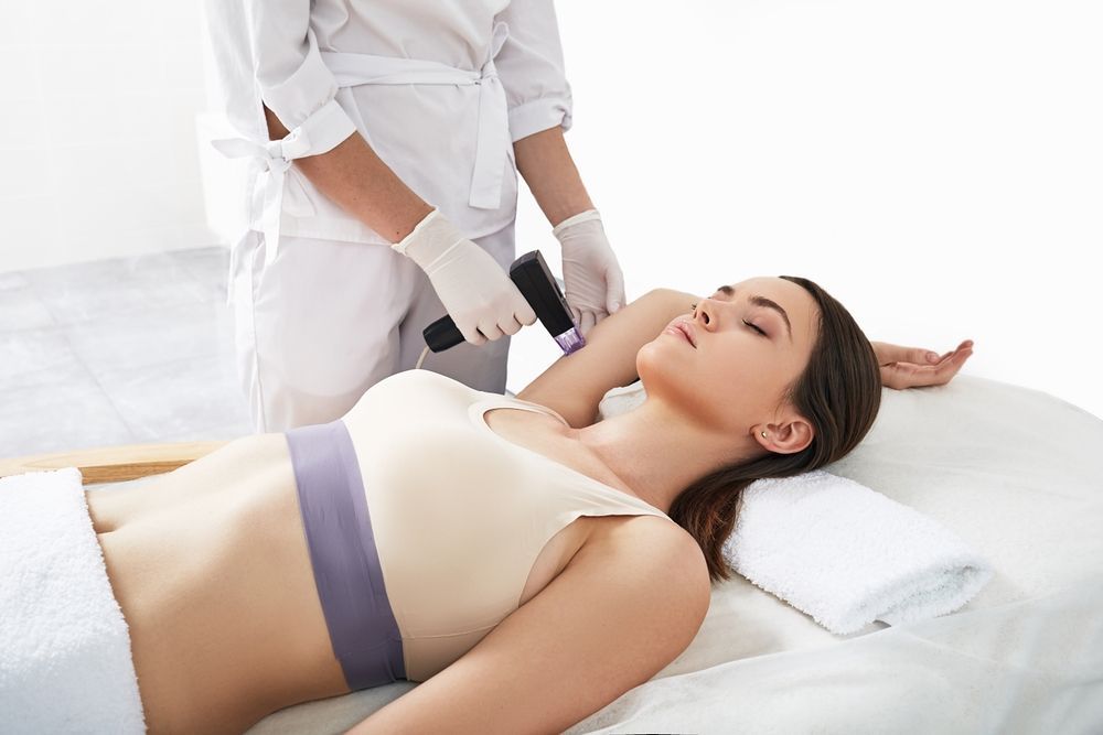 A woman is laying on a bed getting a laser hair removal treatment.
