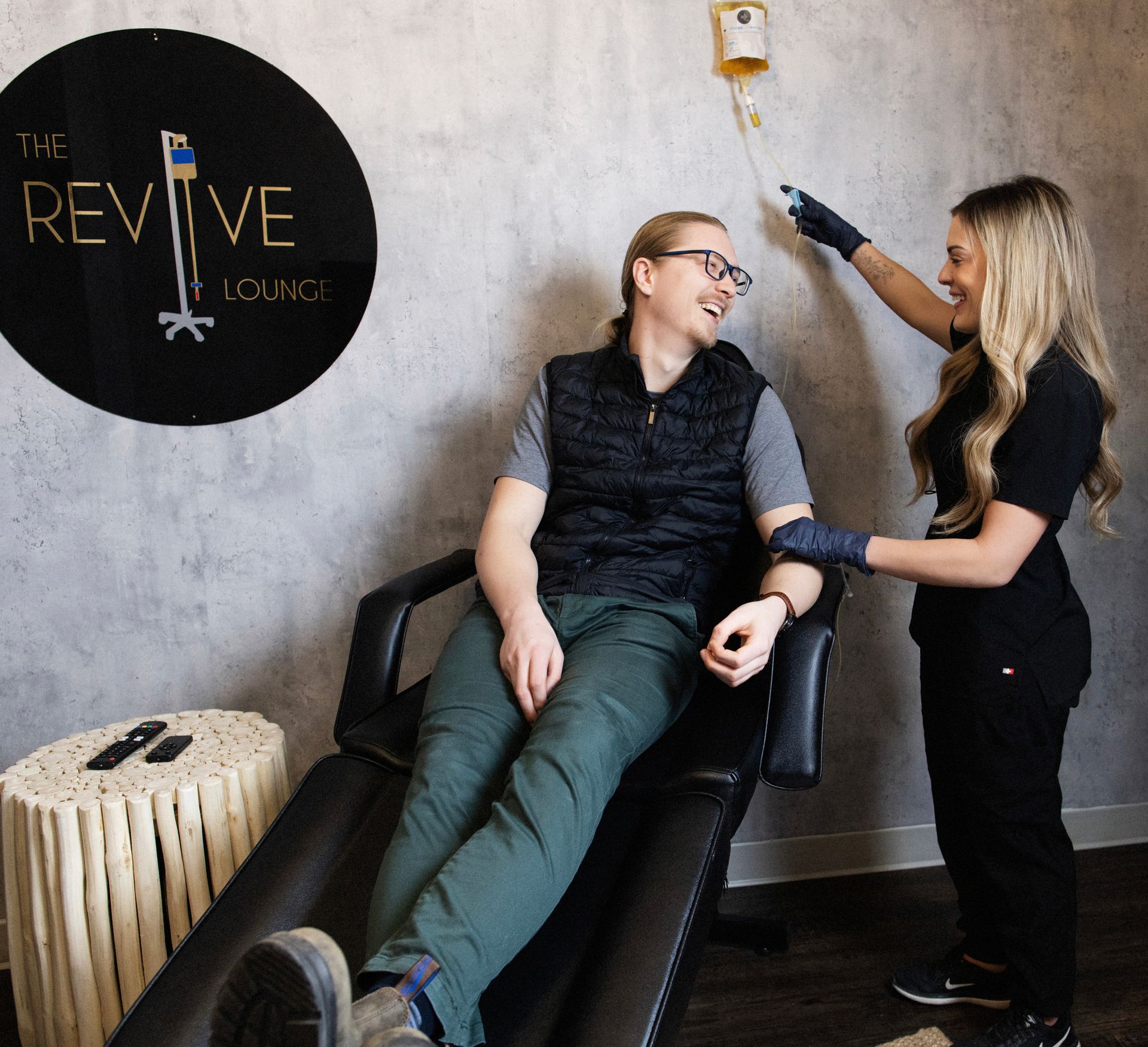a man is sitting in a chair with a woman standing next to him at the revive lounge