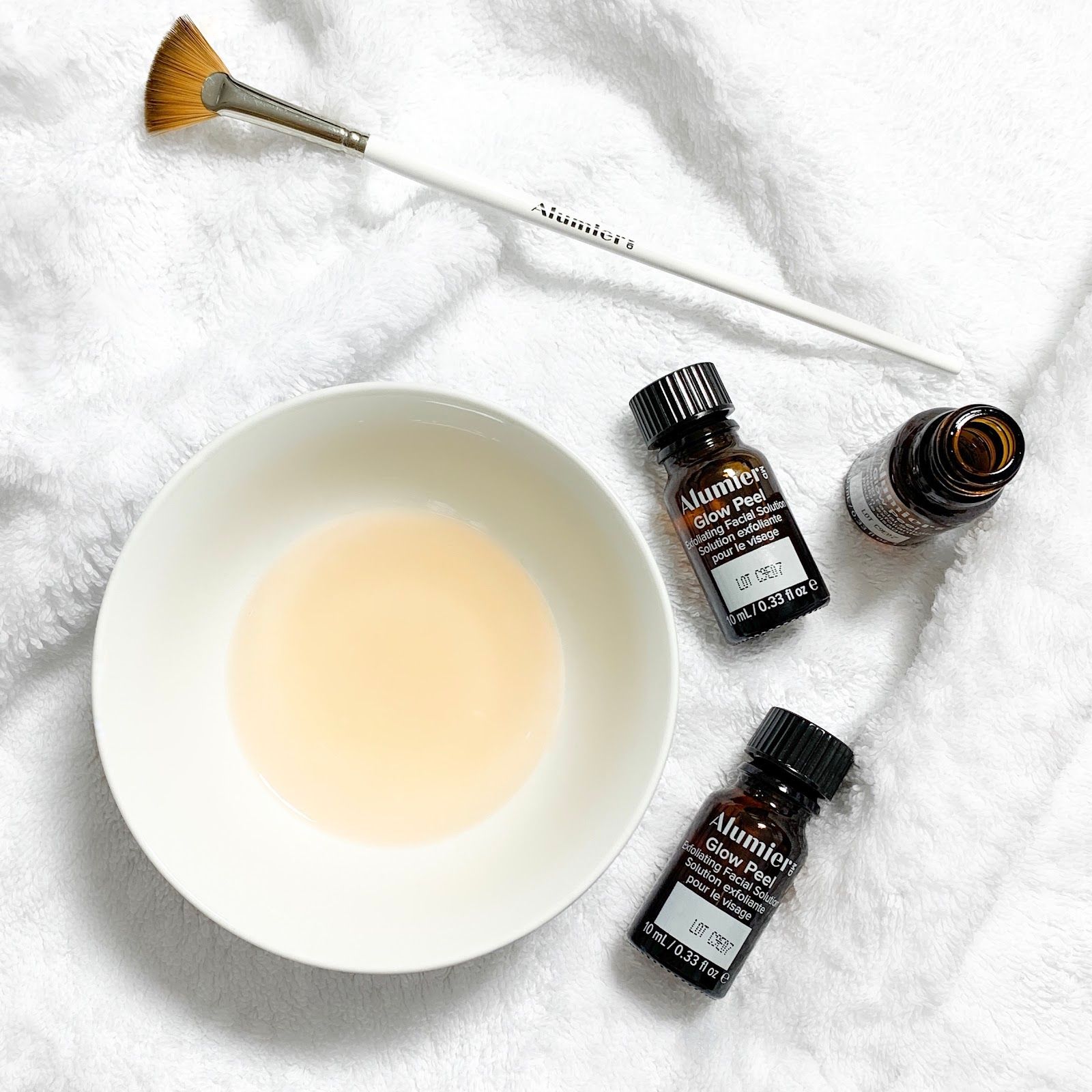 A bowl of liquid next to three bottles of liquid and a brush.