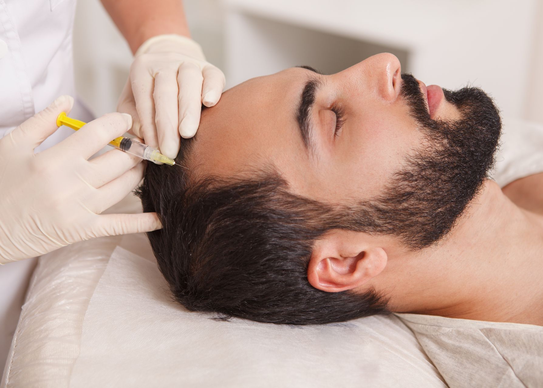 a man with a beard is getting a botox injection in his head .