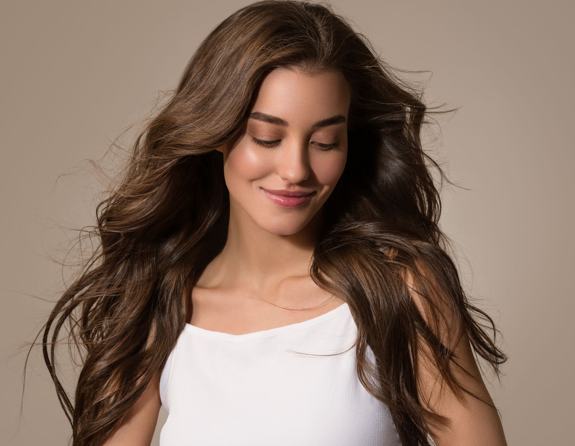 a woman with long brown hair is wearing a white tank top .