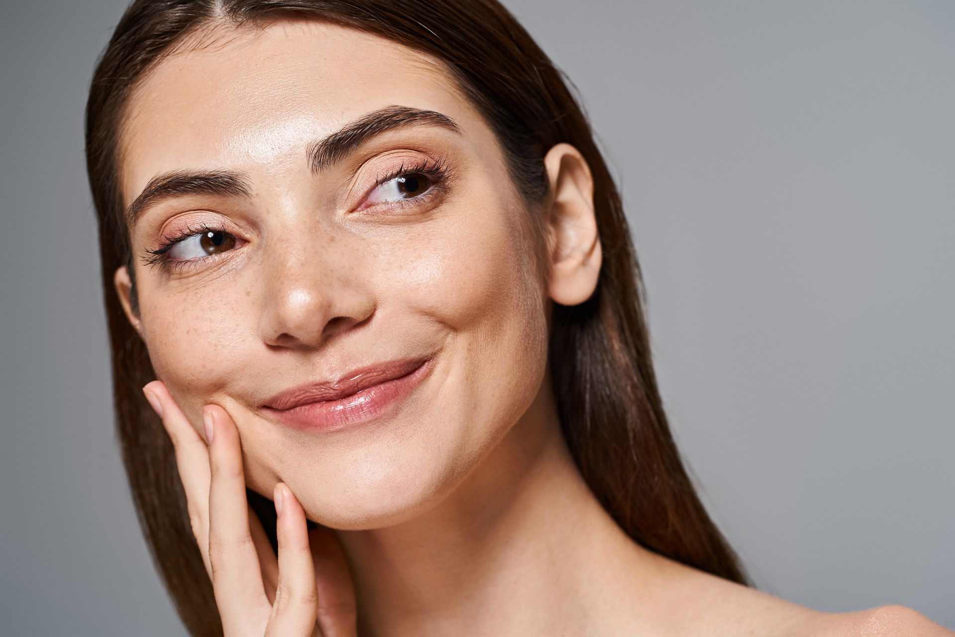 A woman is touching her face with her hand and smiling.