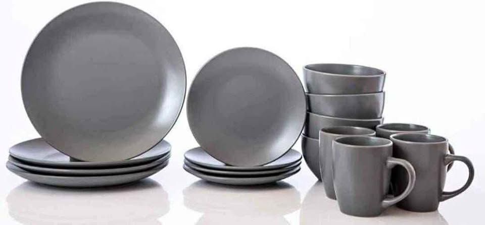 Juego de vajilla gris: platos, cuencos y tazas sobre una superficie blanca.