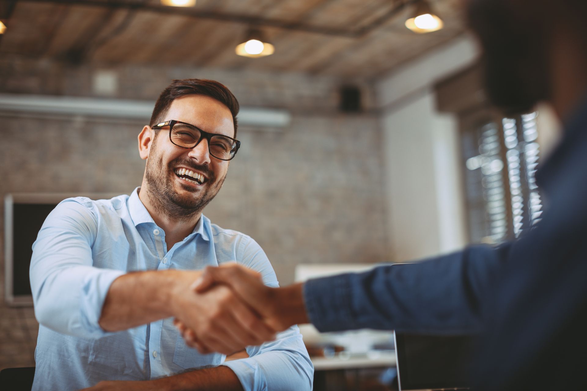 Man in glasses smiling, shaking hands with another person in an office.