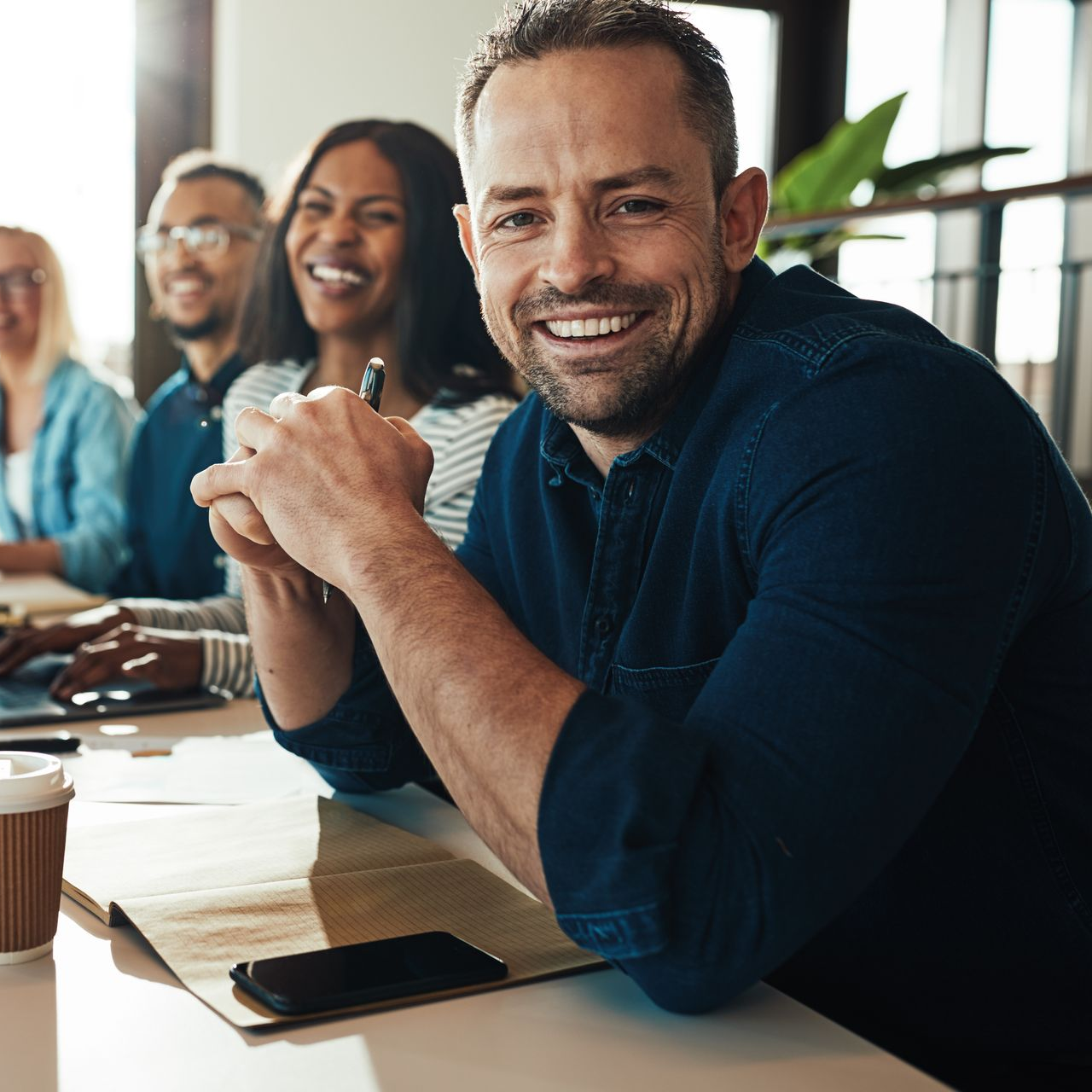 Man smiling at camera in office meeting with colleagues. Man smiling at camera in office meeting with colleagues.