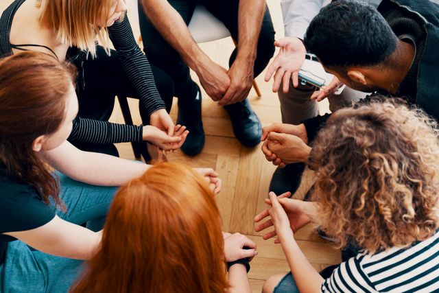 People in a circle, hands clasped, engaged in a group discussion.