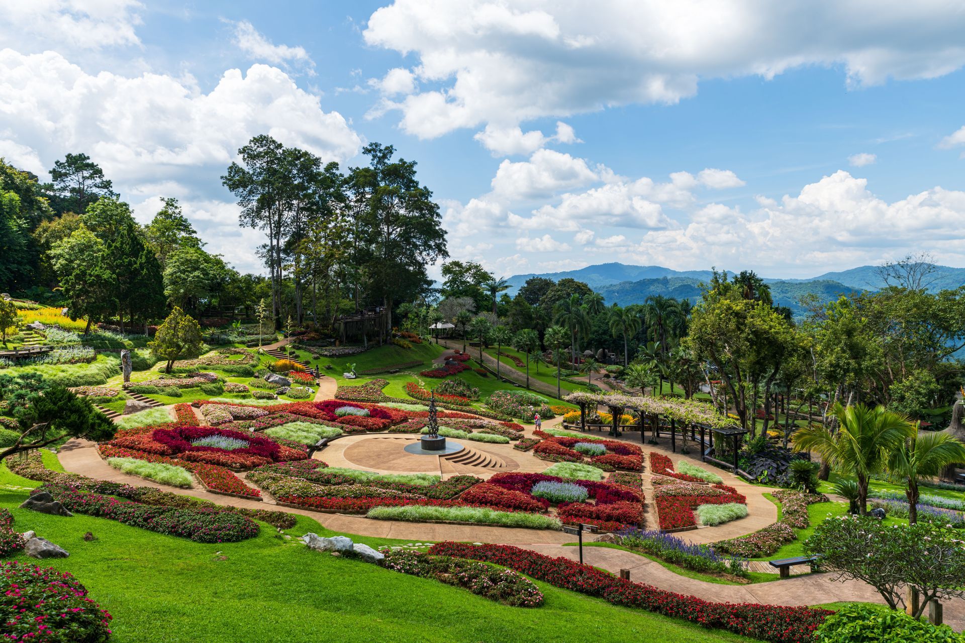 Colorful flower garden with winding paths and lush green hills under a bright sky