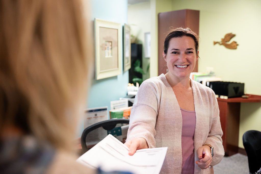 Woman smiling and handing papers across a desk at Robert A. Lantzy, DMD, LCC  in Newtown, PA
