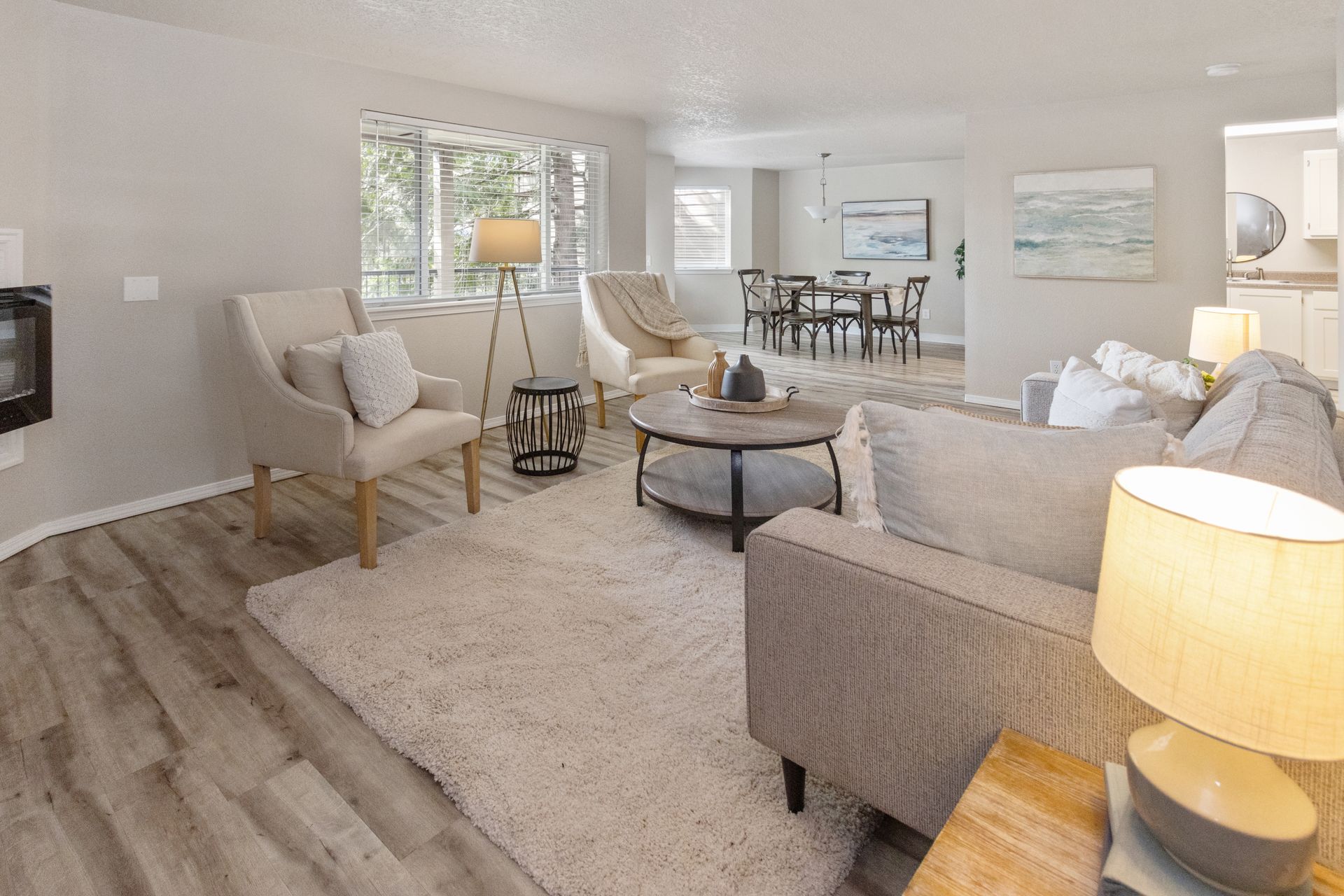 Living room with light gray walls, wood-look floor, neutral furniture, and dining area visible.