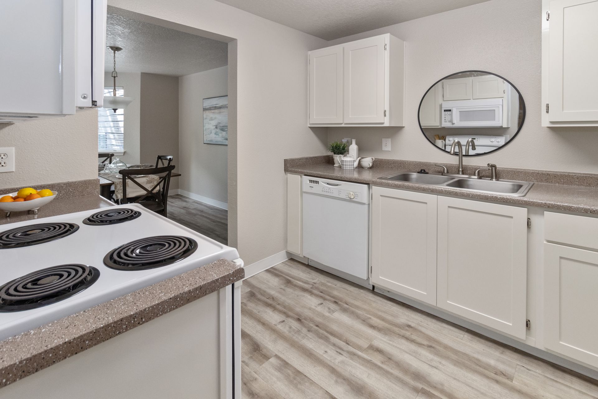 A kitchen with white cabinets, countertops, appliances, and light wood flooring.