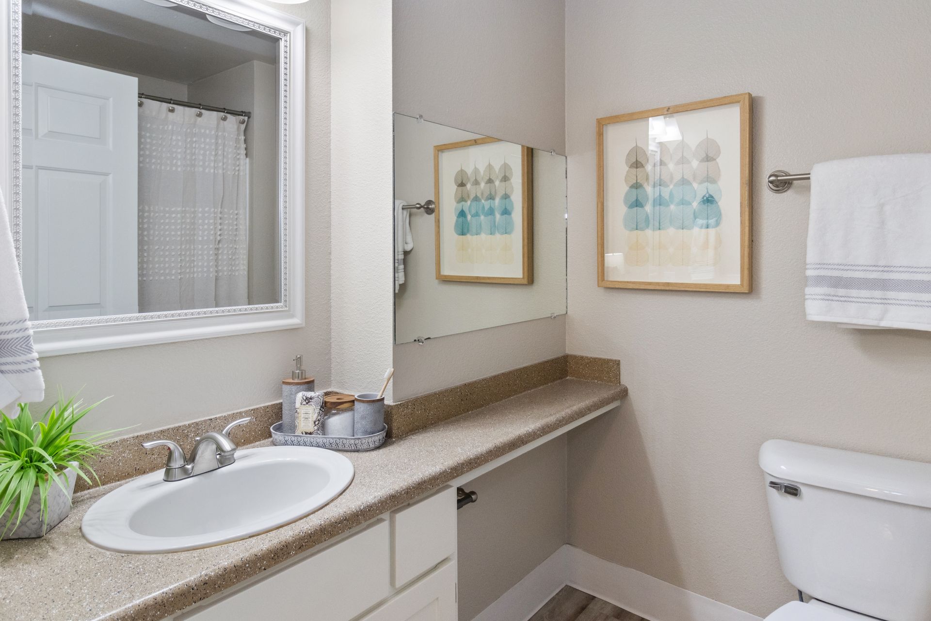 Bathroom with a sink, toilet, mirror, and decorative wall art in neutral tones.