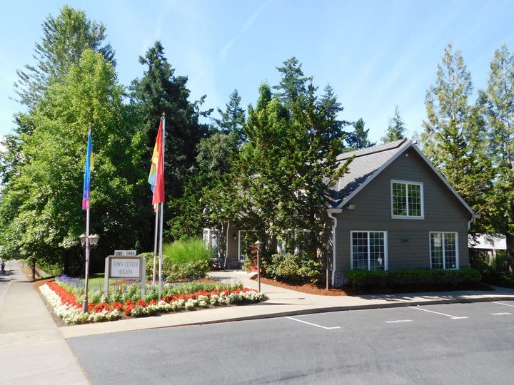 Small green building with flags and a garden, on a sunny day.
