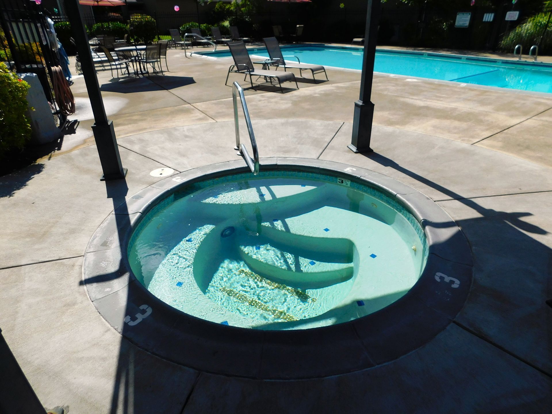 Circular water feature at poolside, with a handrail. Pool and lounge chairs in the background.