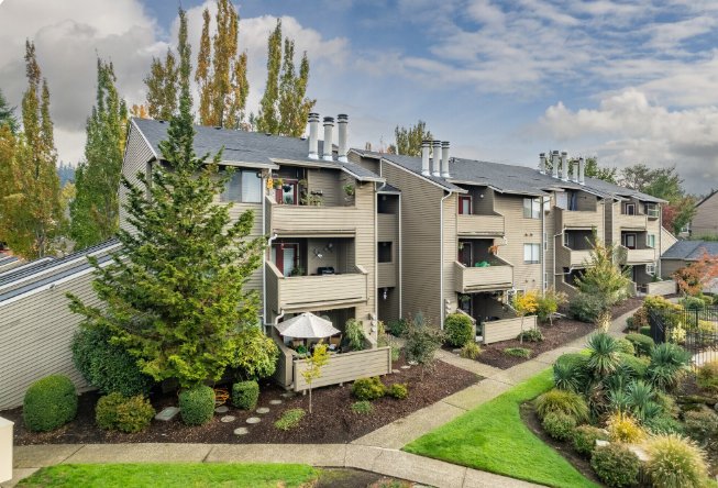 Apartment buildings with balconies and green landscaping on a sunny day.