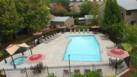 Pool area with lounge chairs, umbrellas, and hot tub.