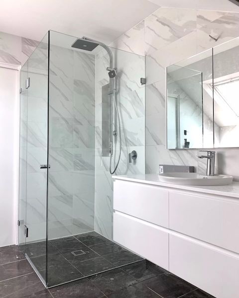 A bathroom with a walk in shower , toilet , sink and mirror.