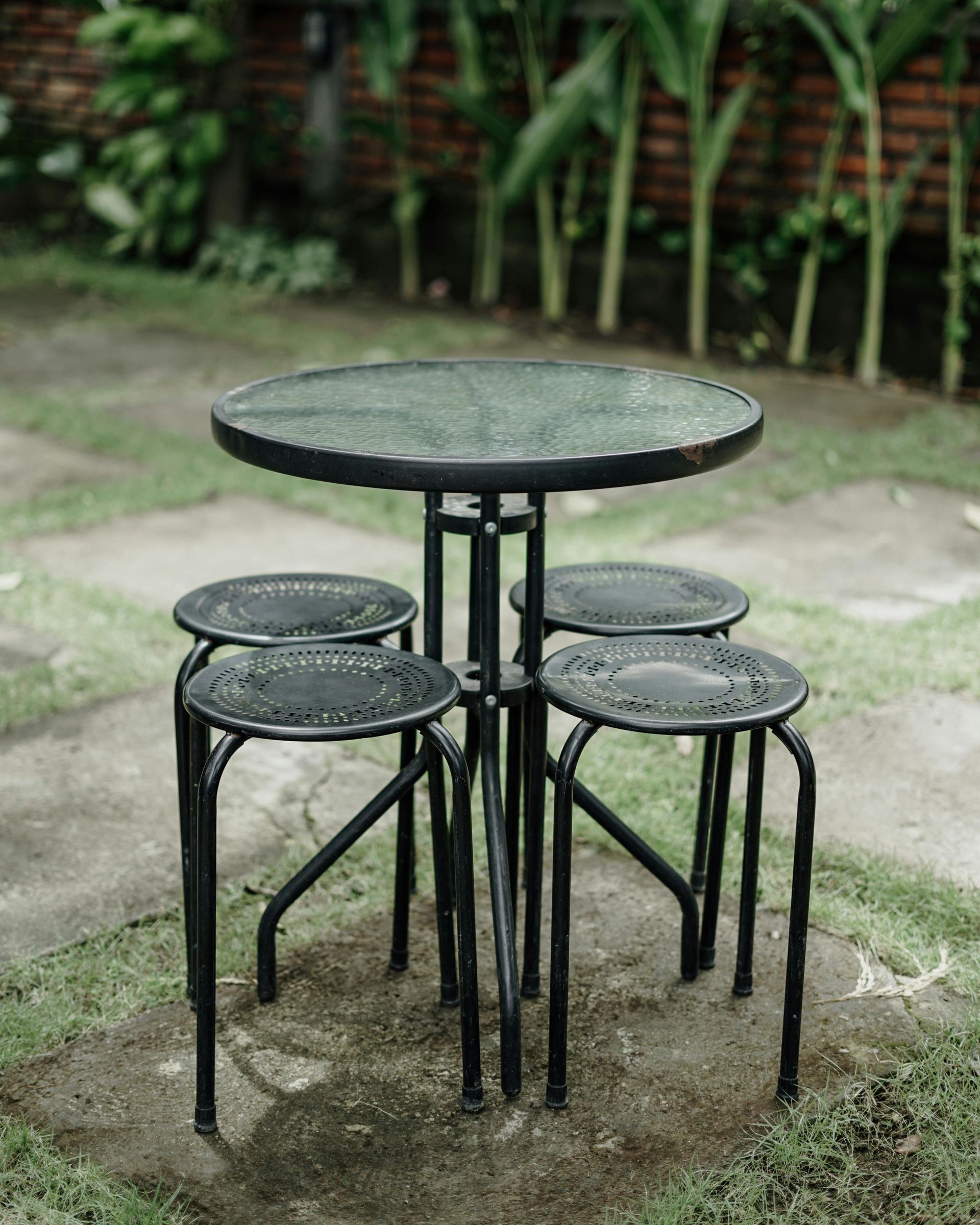 A round table and stools are sitting on the ground in a garden.