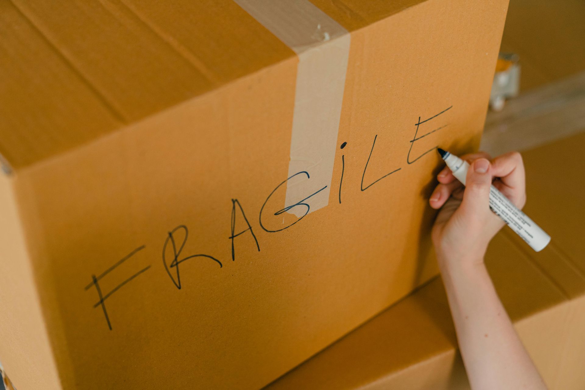 A person is writing fragile on a cardboard box with a marker.