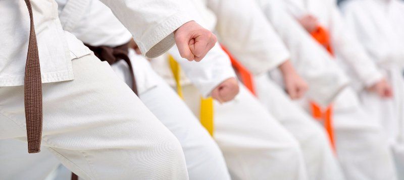 A row of people in white karate clothing with orange or yellow belts