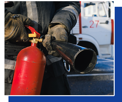 A fireman is holding a red fire extinguisher in front of a fire truck with the number 27 on it.