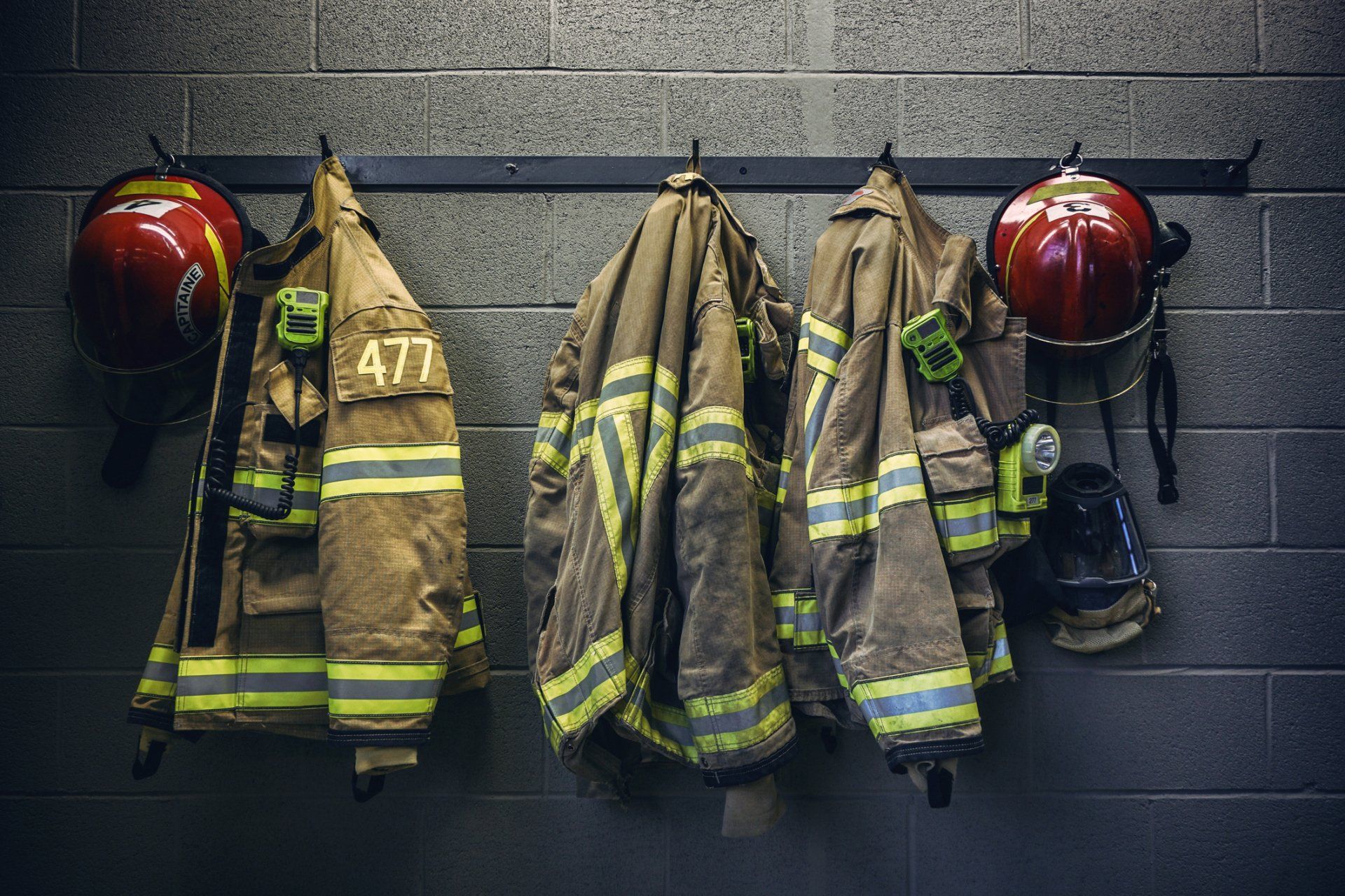 A row of firefighter 's uniforms and helmets hanging on a wall.
