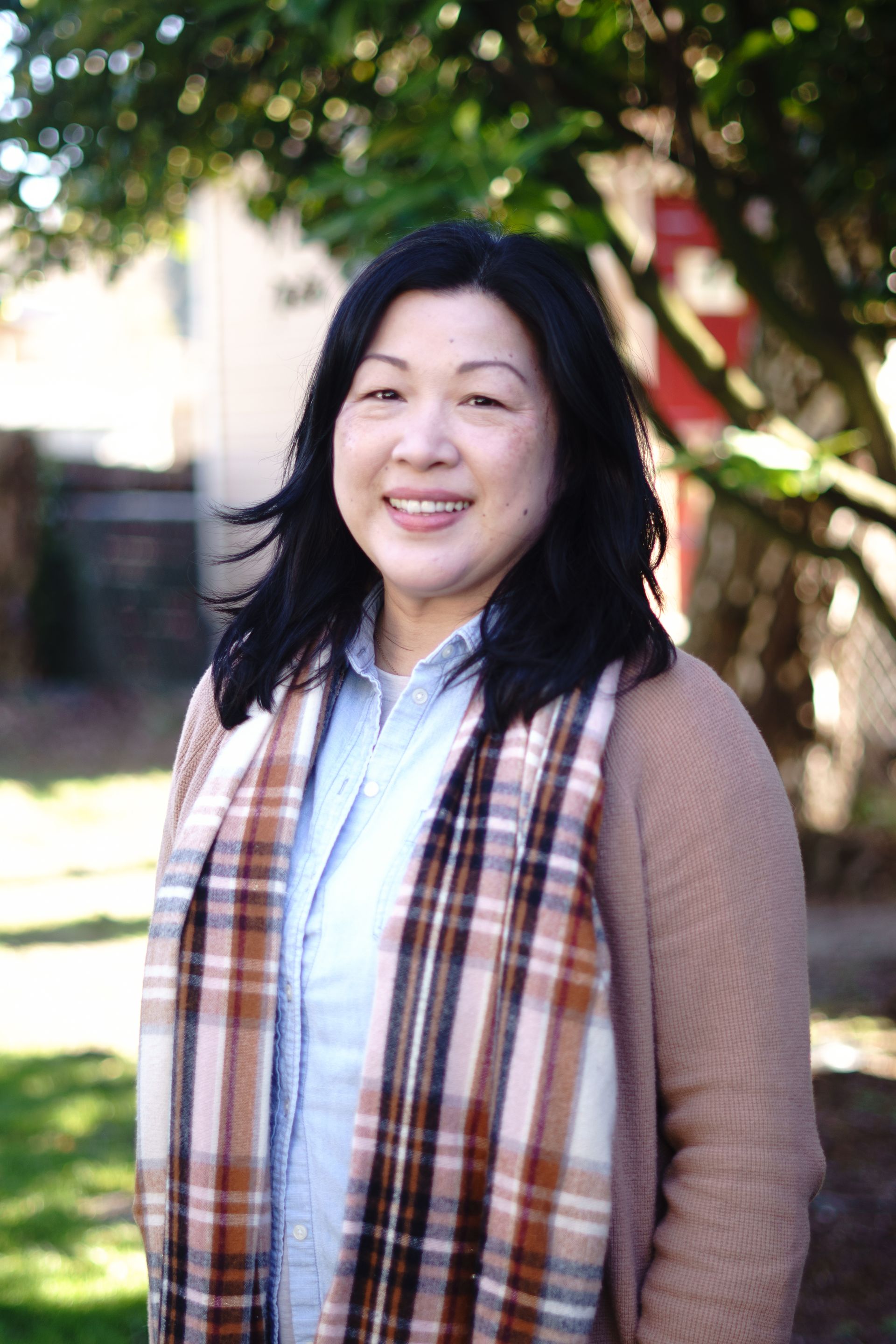 A woman wearing a scarf and a sweater is standing in front of a tree.