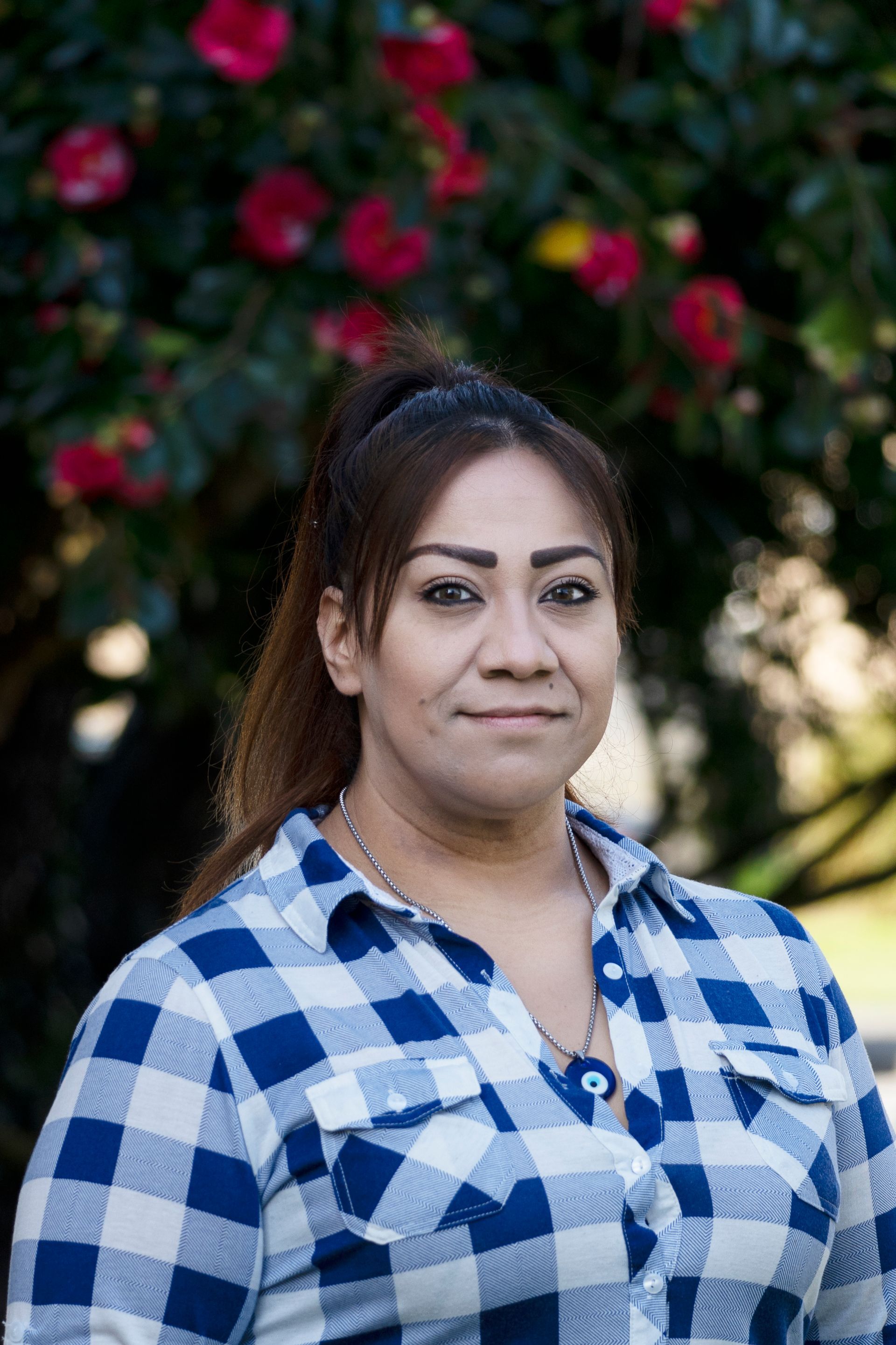 A woman in a plaid shirt is standing in front of a tree with red flowers.