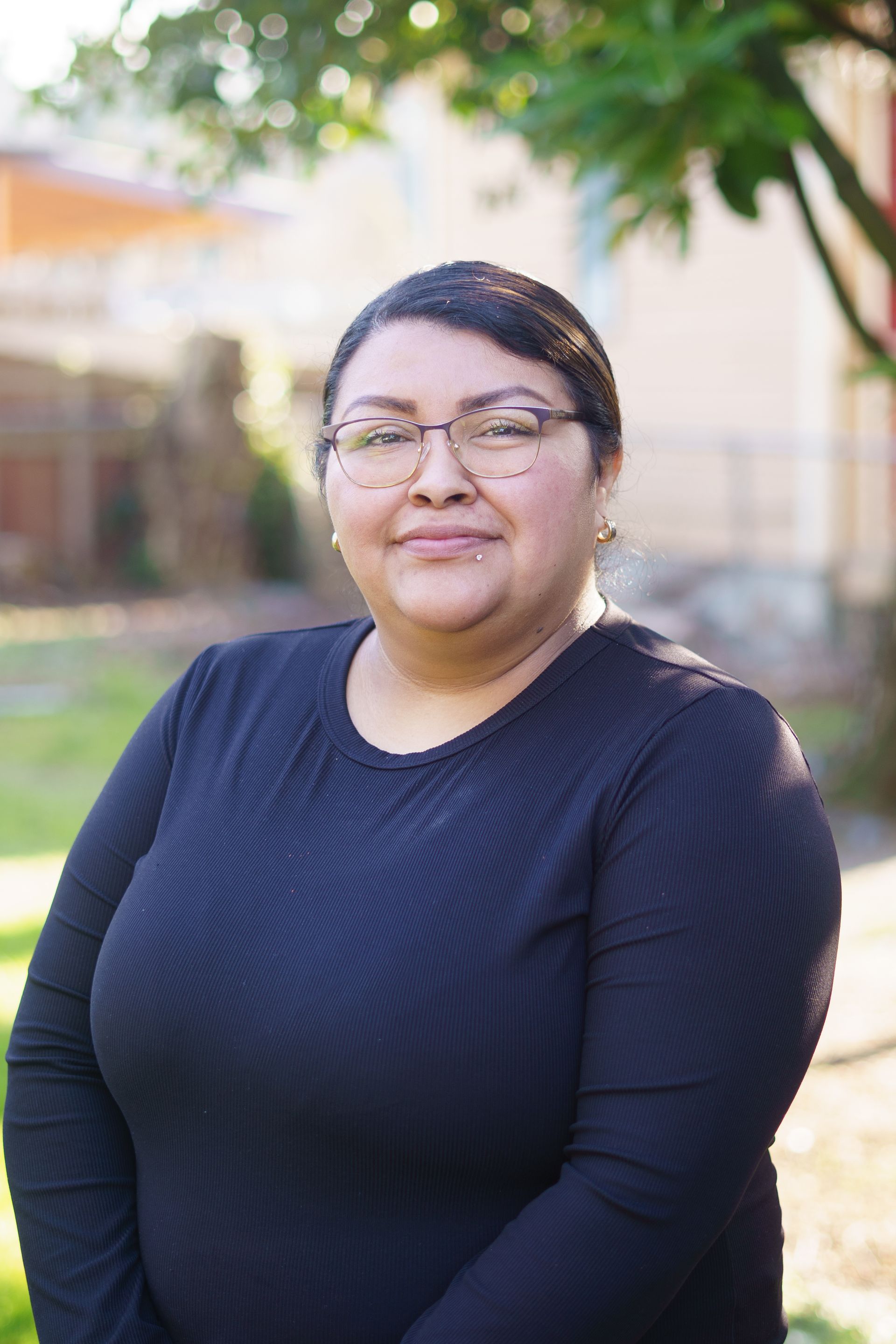 A woman wearing glasses and a black shirt is standing in front of a tree.