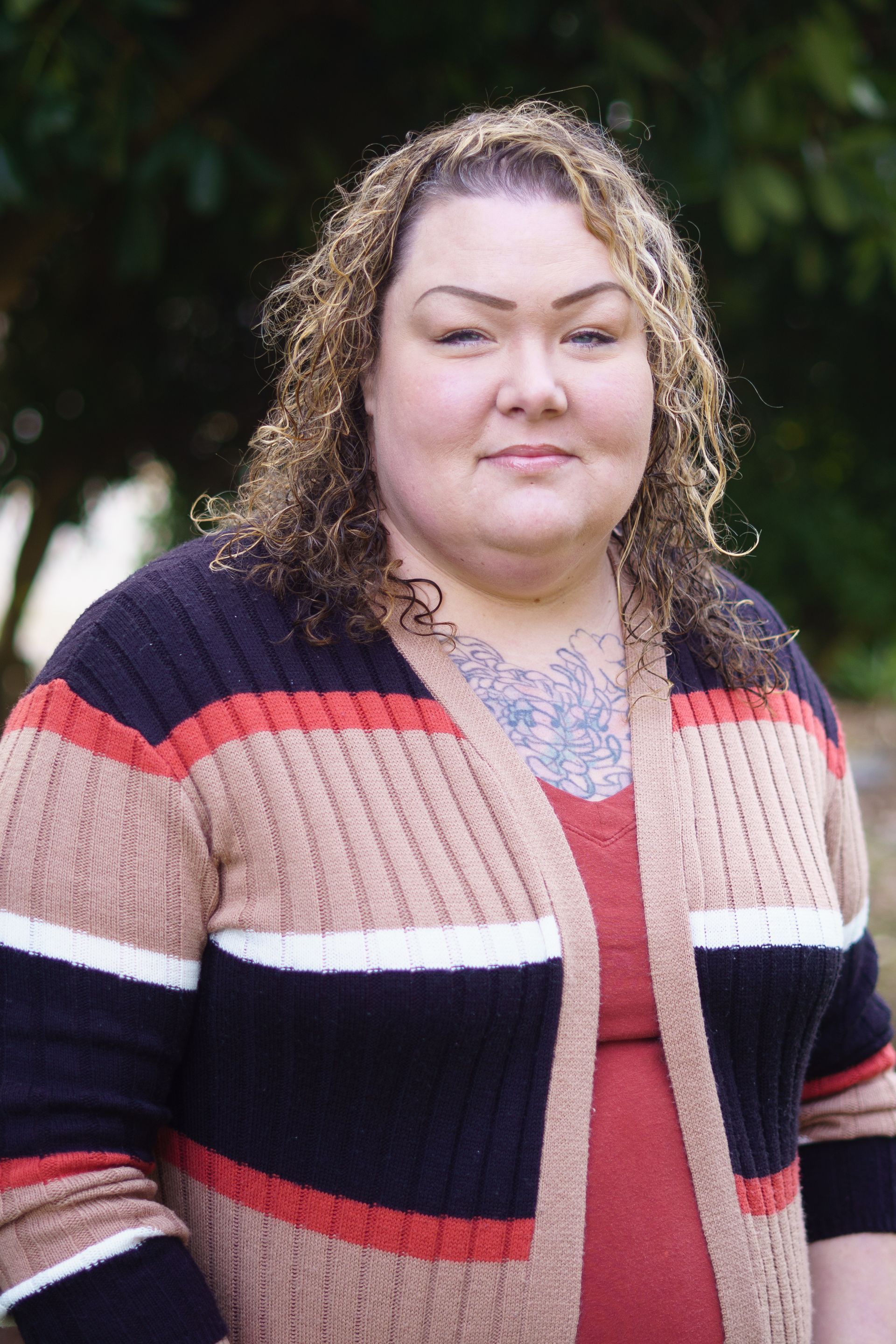 A woman in a striped sweater is standing in front of a tree.