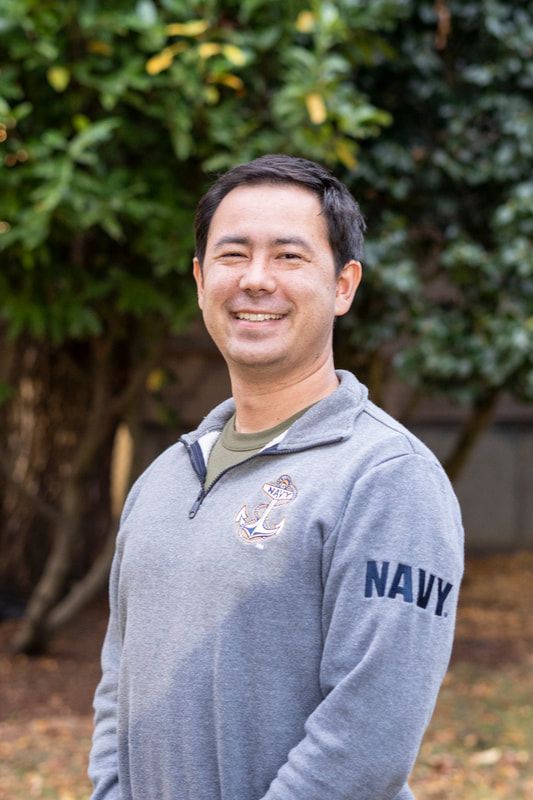A man wearing a gray navy sweatshirt is smiling for the camera.