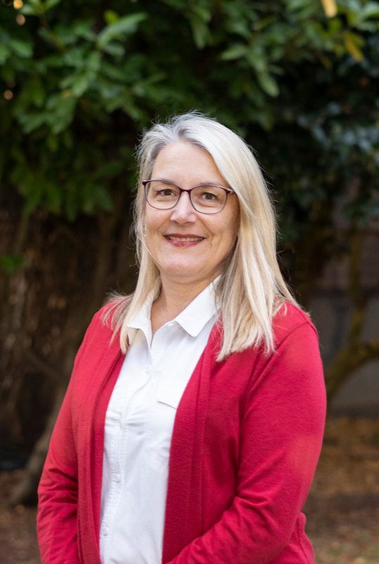 A woman wearing glasses and a red sweater is standing in front of a tree.