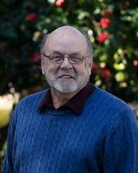 A man with a beard and glasses is wearing a blue sweater.