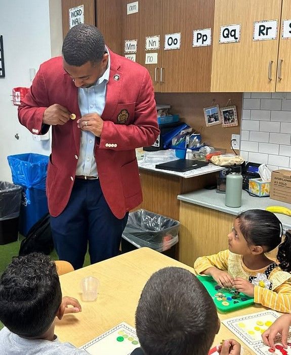 A man in a red jacket is talking to a group of children
