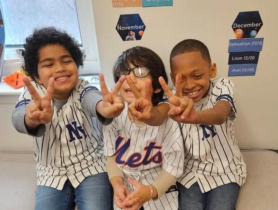 Three young boys wearing ny mets jerseys are giving peace signs