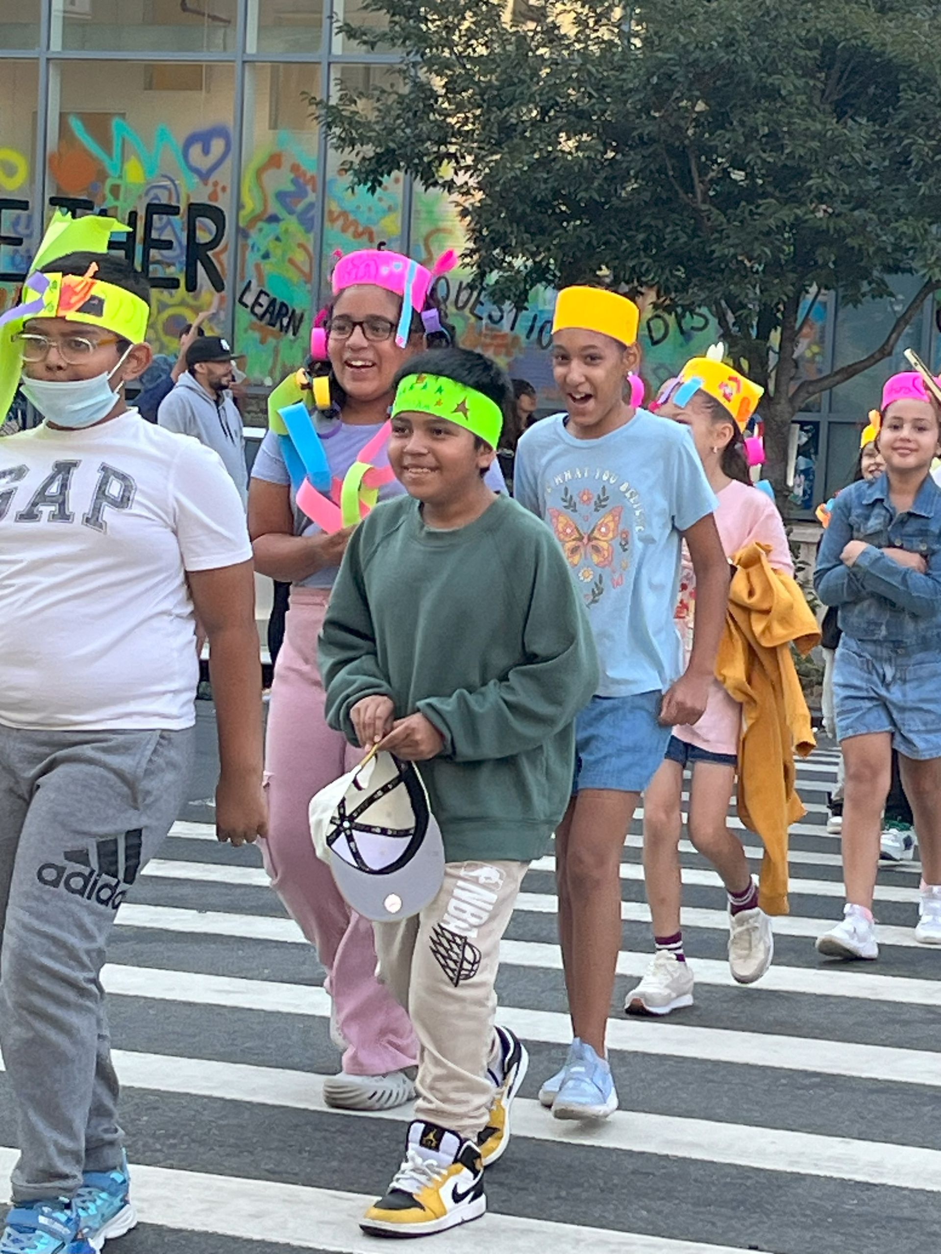 A group of children are crossing a street wearing colorful hats.