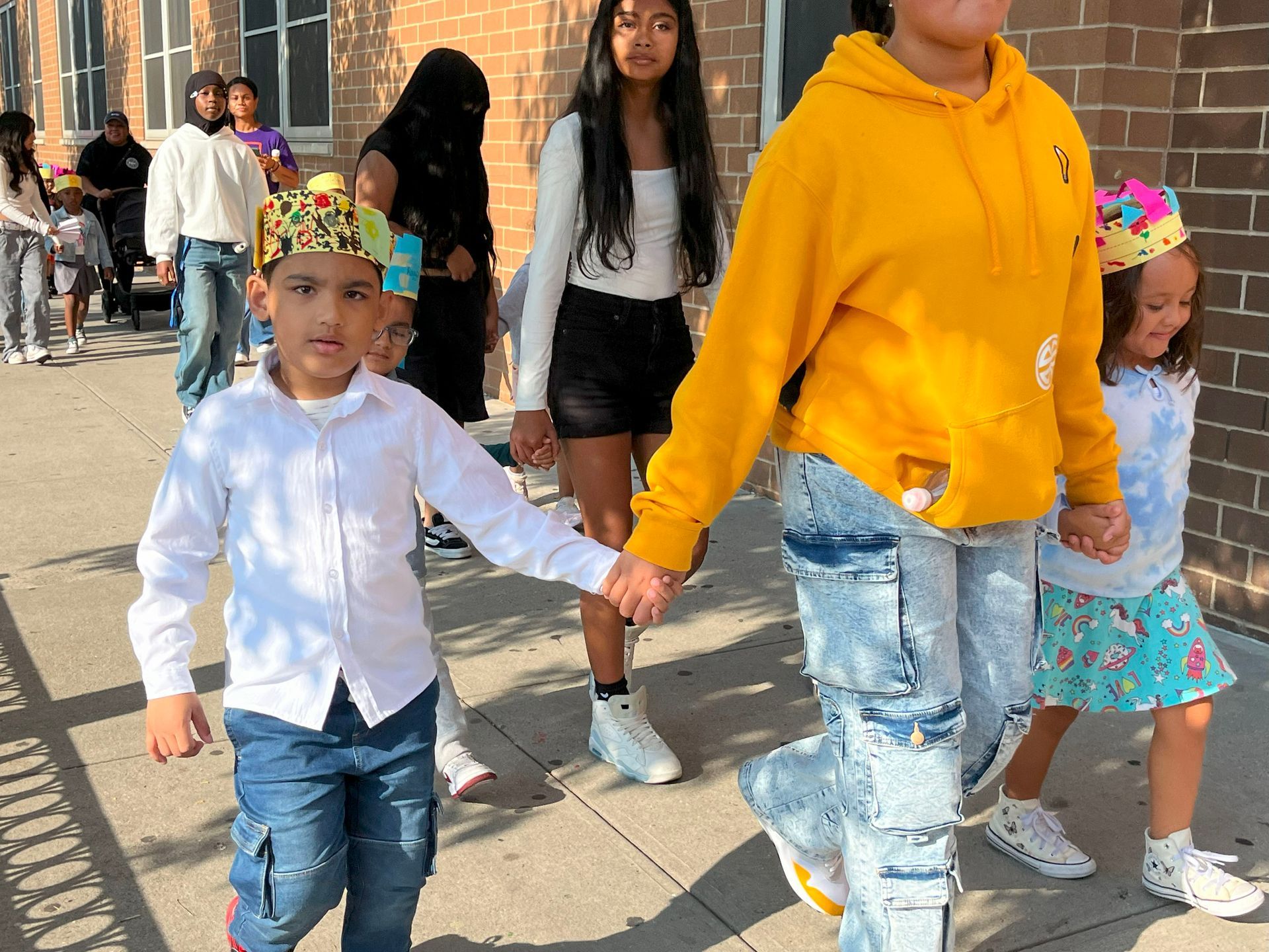 A group of children are walking down a sidewalk holding hands