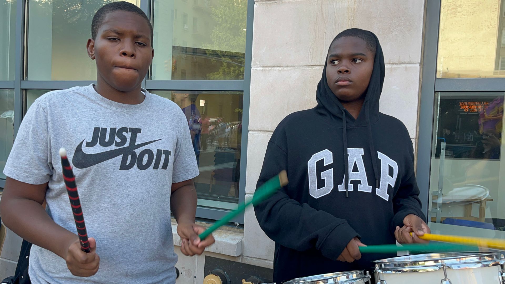 Two boys are playing drums and one has a gap sweatshirt on