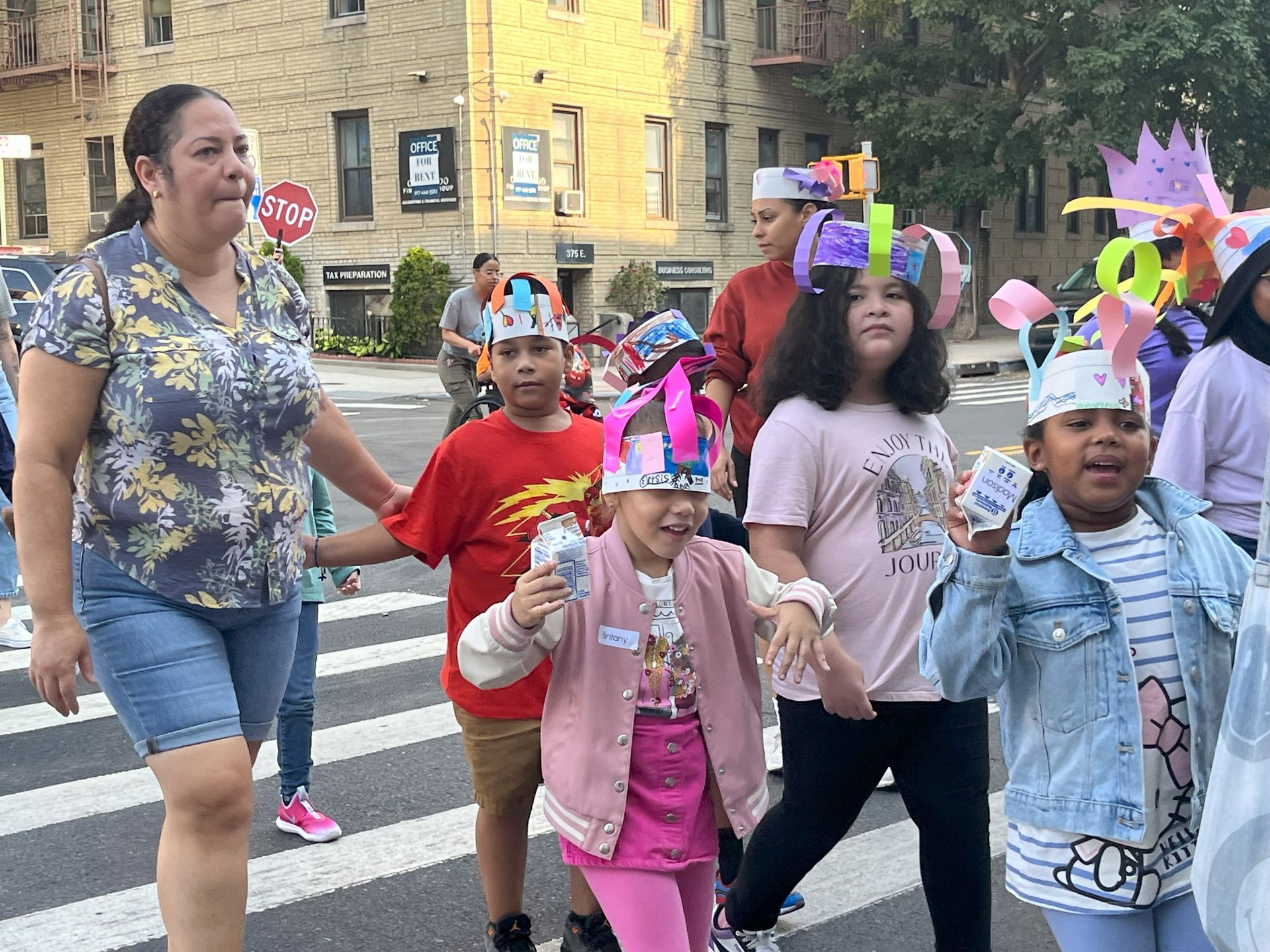 A group of children wearing paper hats are crossing the street