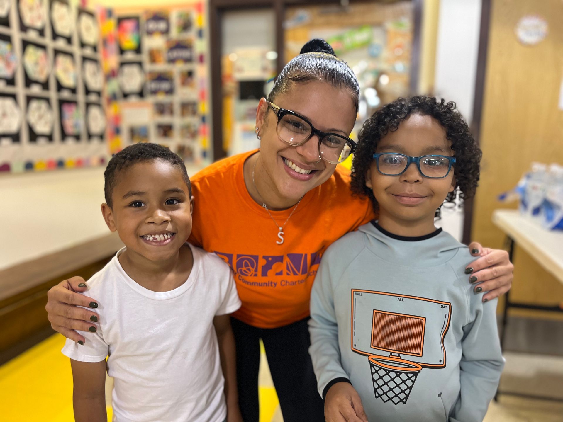 A woman in an orange shirt is posing for a picture with two children