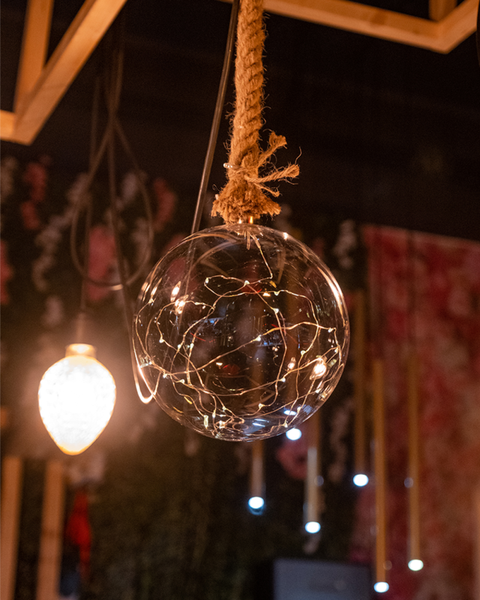 Lampadario a forma di sfera di vetro con luci a catena appese a una corda, altre luci e uno sfondo floreale.