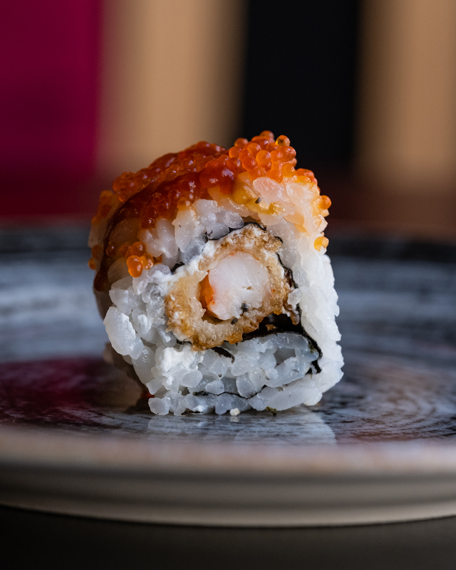 Rotolo di sushi con tempura di gamberi, guarnito con uova d'arancia, su un piatto.
