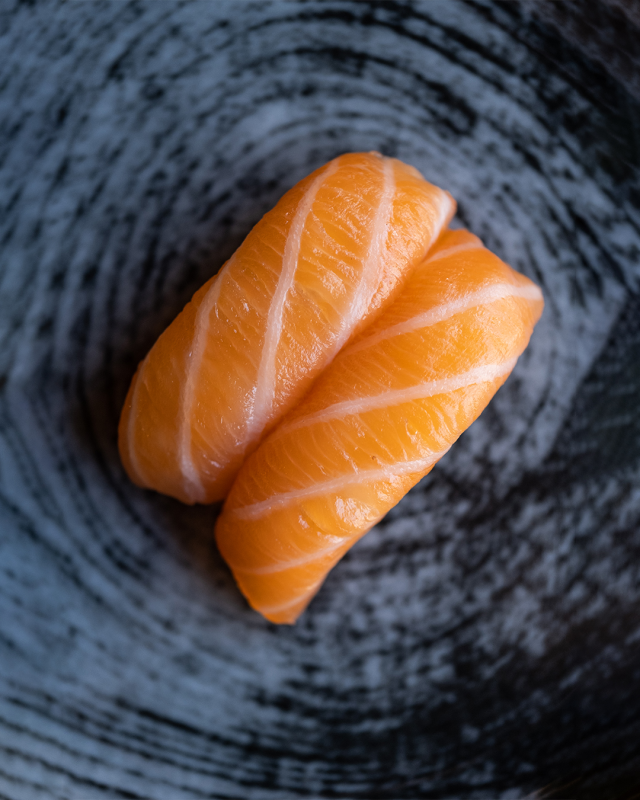 Due pezzi di sushi nigiri al salmone su un piatto blu testurizzato.