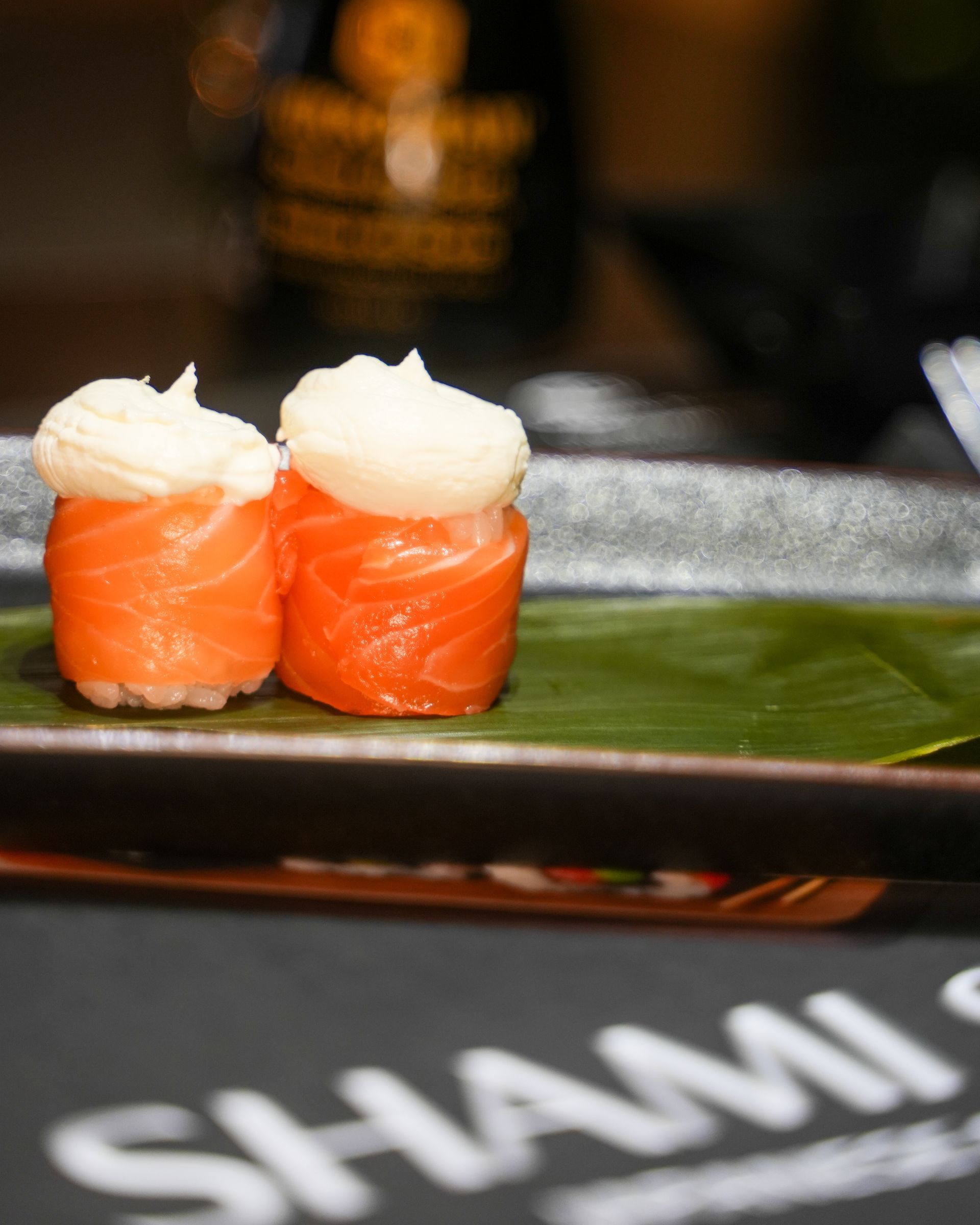 Involtini di sushi con salmone, avocado e guarnizione croccante su un piatto bianco.