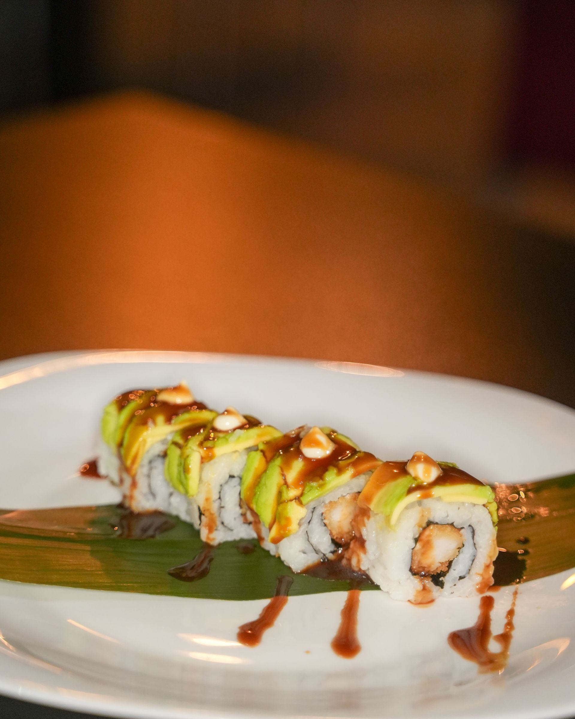 Sushi guarnito con guarnizione bianca, pistacchi e un filo di salsa su un piatto bianco.