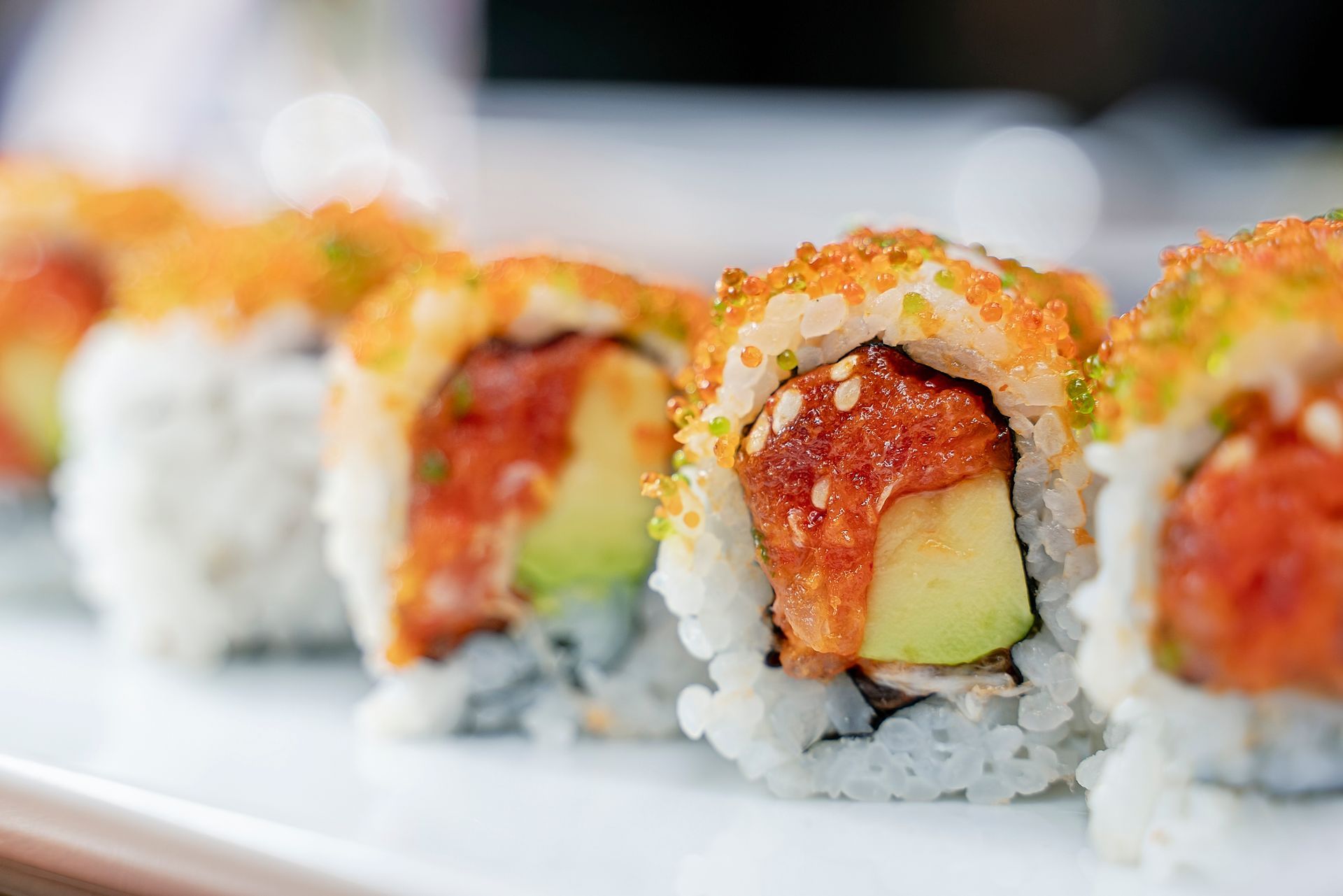 Involtini di sushi, primo piano con avocado, tonno piccante e uova d'arancia su un piatto bianco.