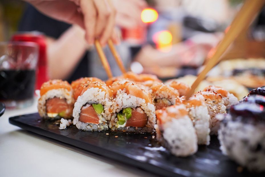 Involtini di sushi con salmone e avocado su un piatto nero, con le bacchette inserite.
