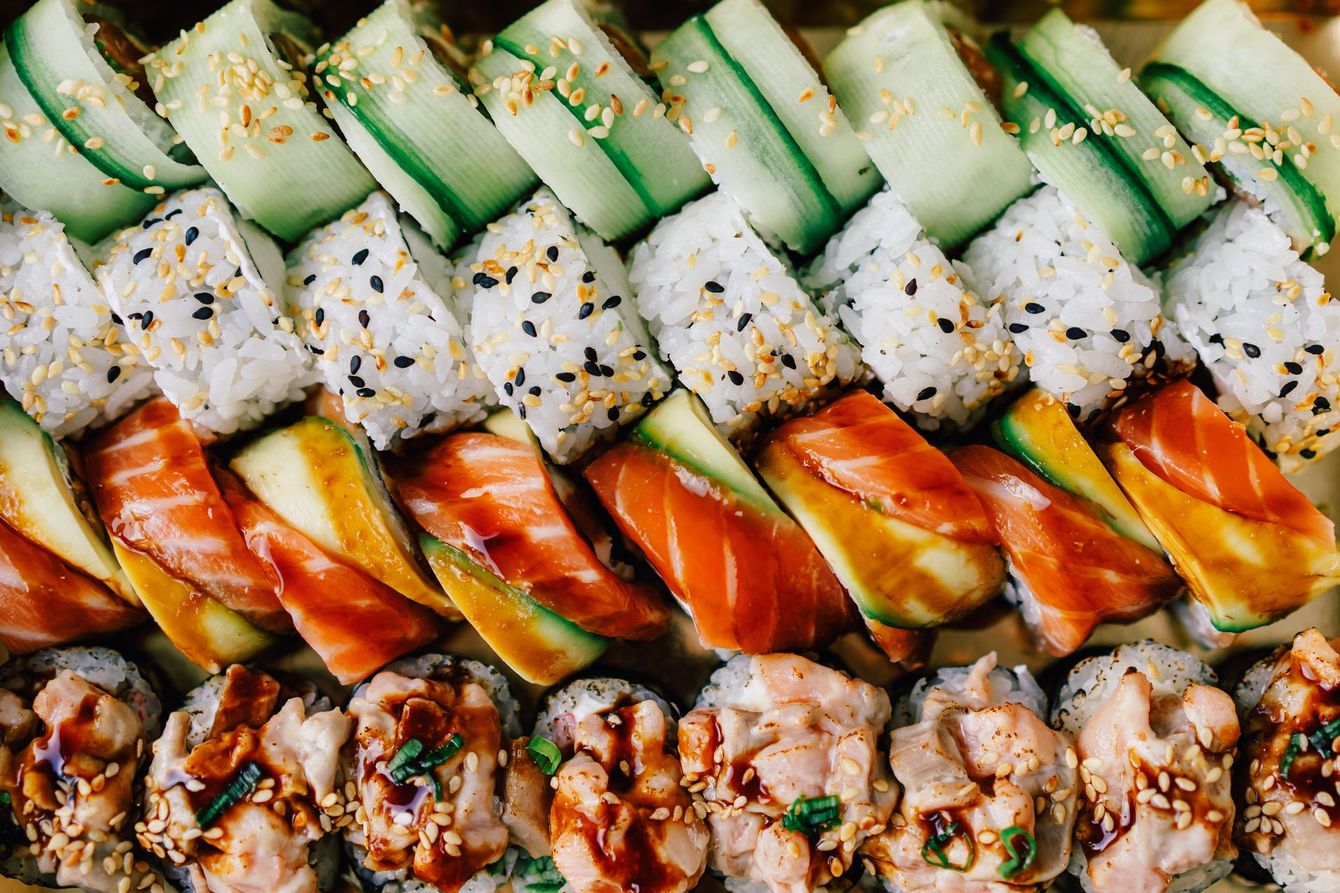 Piatto di sushi con vari involtini, tra cui salmone, cetriolo e semi di sesamo.