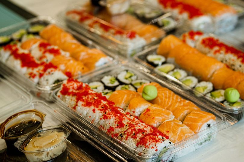 Rotoli di sushi in contenitori di plastica trasparente con salsa di soia e wasabi.