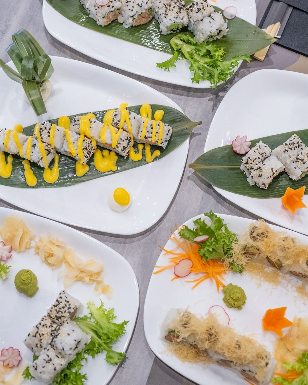 Piatti di involtini di sushi con vari condimenti e guarnizioni, disposti su un tavolo.